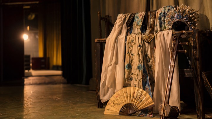 Peking opera robe, headdress, fan, and stage instruments under warm light