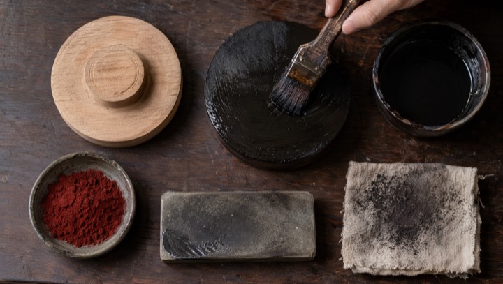 Brush applying black lacquer to a wooden lacquerware base with pigments and tools nearby
