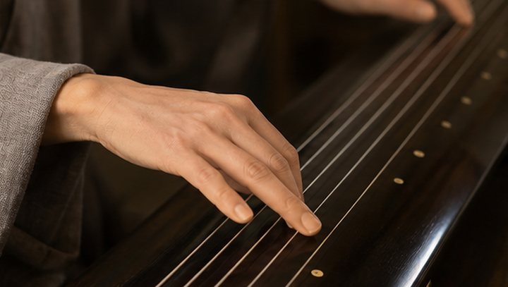 Hands plucking and pressing guqin strings during focused practice